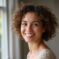 Portrait of a young, enthusiastic woman with curly hair, smiling warmly, representing community engagement.
