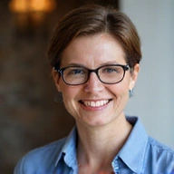 Portrait of a smiling woman with short brown hair, wearing glasses, and a blue shirt, exuding professionalism and approachability.